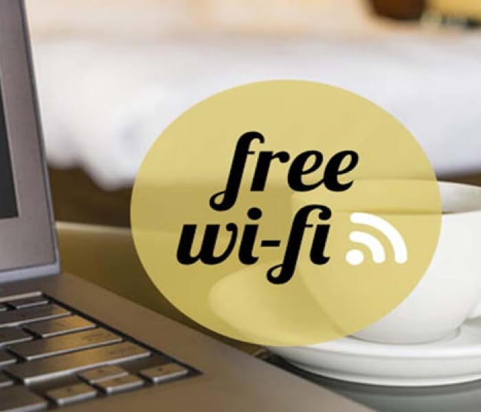Tastiera di laptop con tazza di caffè e logo "free wi-fi" su sfondo sfocato di un tavolo.