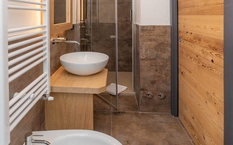Small bathroom featuring a white sink, shower with glass walls, toilet, and wooden accents on the walls and floor.