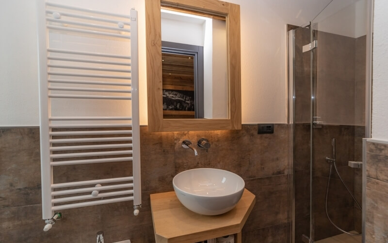 A clean bathroom featuring a white sink, towel rack, mirror, shower with glass door, and brown tiled walls.