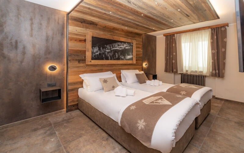 Modern minimalist bedroom with a large bed, wooden wall, forest photograph, and warm earthy tones.