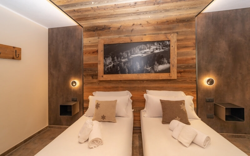 Modern hotel room with twin beds, rustic wood accents, landscape photo, and cozy decor.