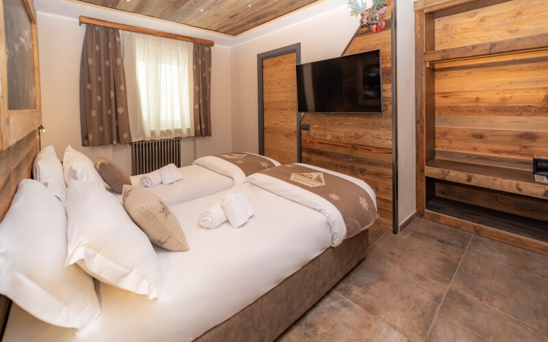 Cozy bedroom with a large bed, TV, wooden ceiling, and warm decor, featuring a window and tiled floor.