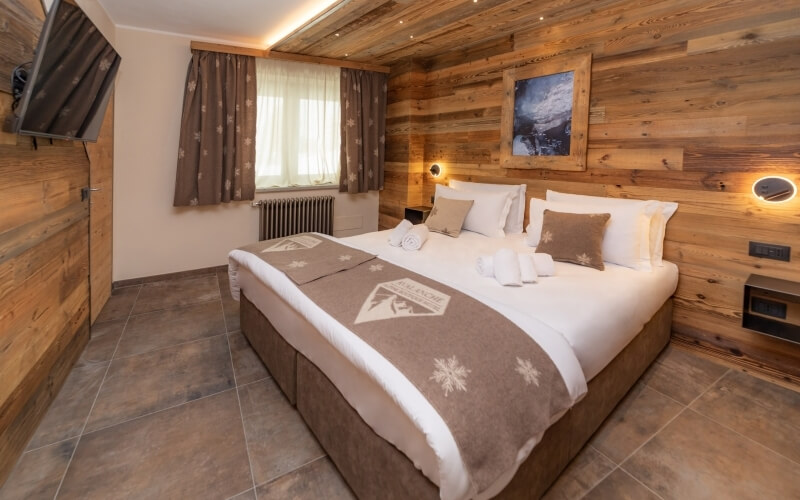 Cozy bedroom with wooden walls, large bed, earthy decor, flat-screen TV, and recessed lighting.