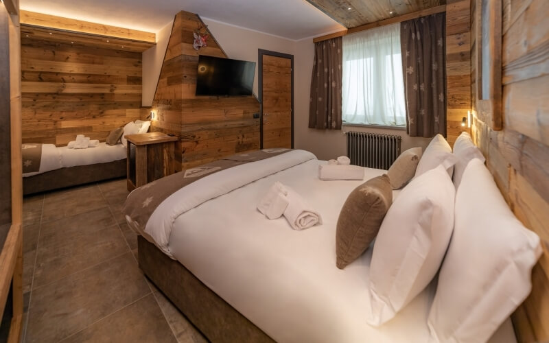 Cozy rustic hotel room with two beds, wooden walls, brown tiles, and natural light from a window with curtains.