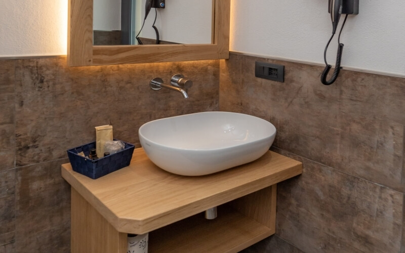 Modern bathroom with a white sink, wooden vanity, mirror, toiletries basket, and sleek faucet.