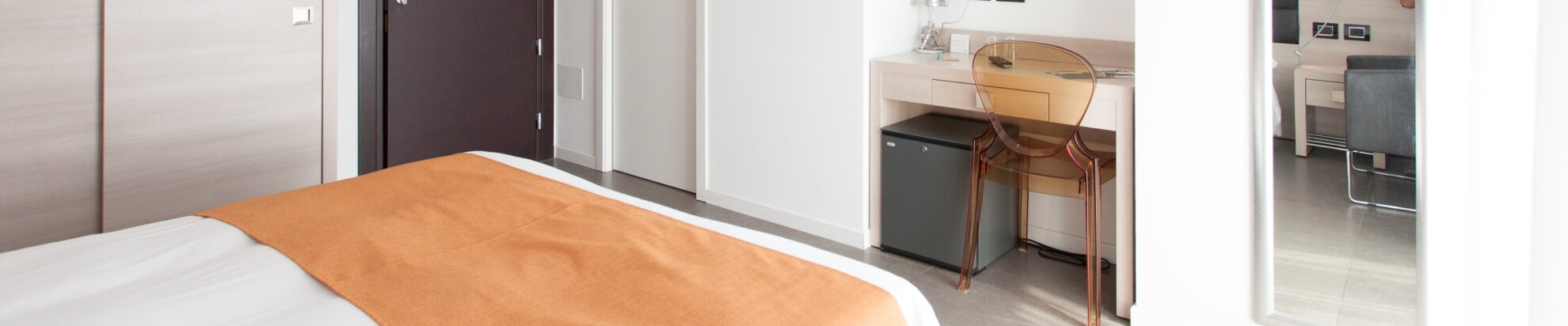Modernes Hotelzimmer mit einem Bett, Schreibtisch, Kühlschrank und natürlichem Licht; minimalistisch und funktional.