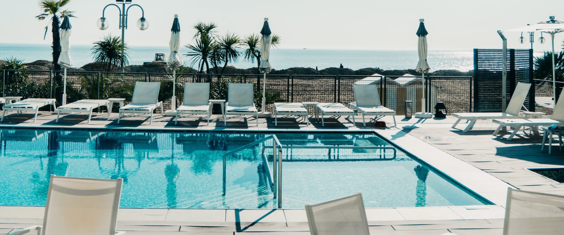 Una scena di un'area piscina con sedie bianche, palme e acqua cristallina che riflette un'atmosfera di relax.