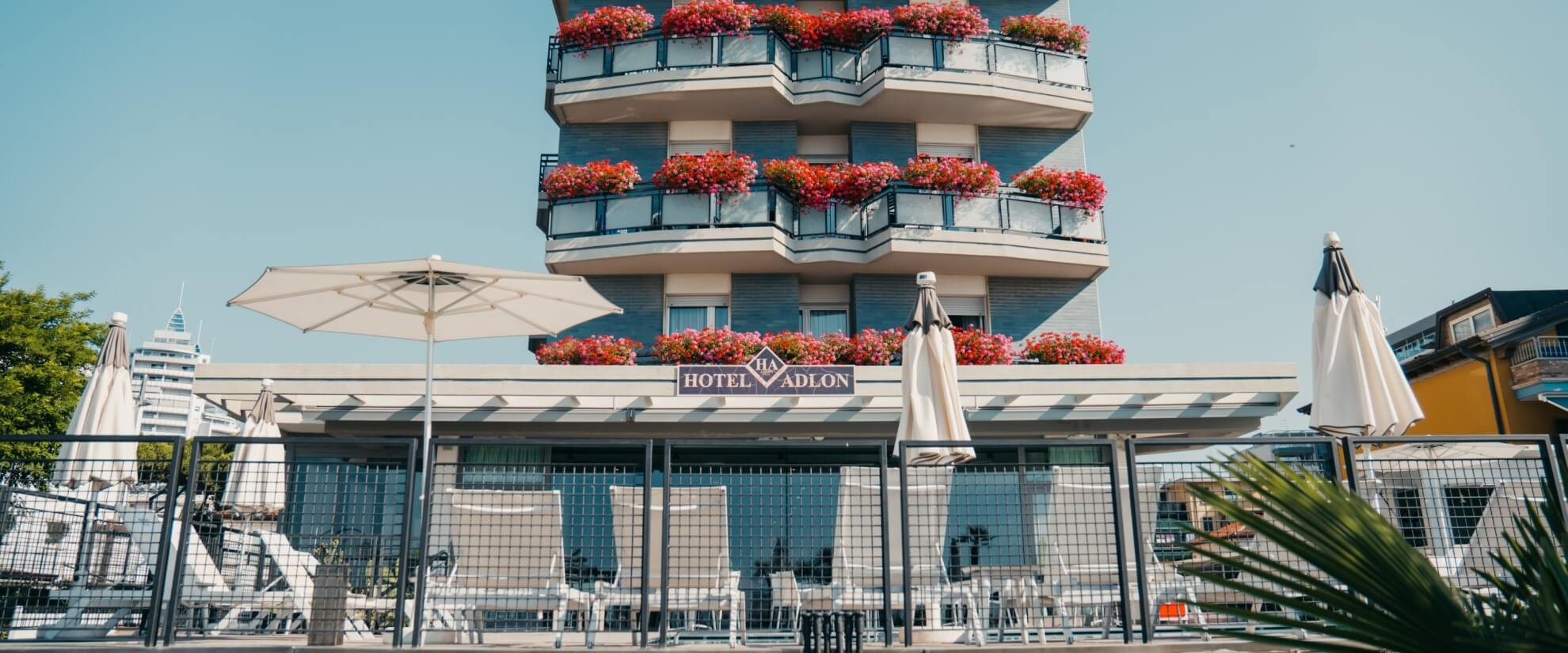 Hotel Vadlon with balcony and patio, surrounded by flowers, greenery, and a clear blue sky, exuding tranquility.