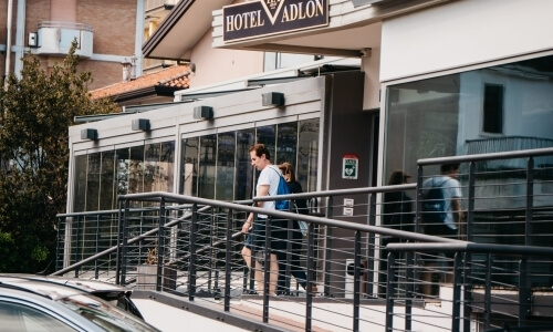 Esterno dell'Hotel Vádlon con insegna, ingresso in vetro, auto parcheggiata e attività pedonale in un ambiente urbano.