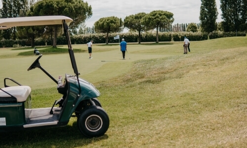 Una scena serena di un campo da golf con un carrello e quattro persone, circondati da erba verde e alberi.