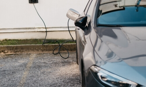 Auto grigia parcheggiata davanti a una presa elettrica, con un cavo di ricarica collegato, in una stazione di ricarica.