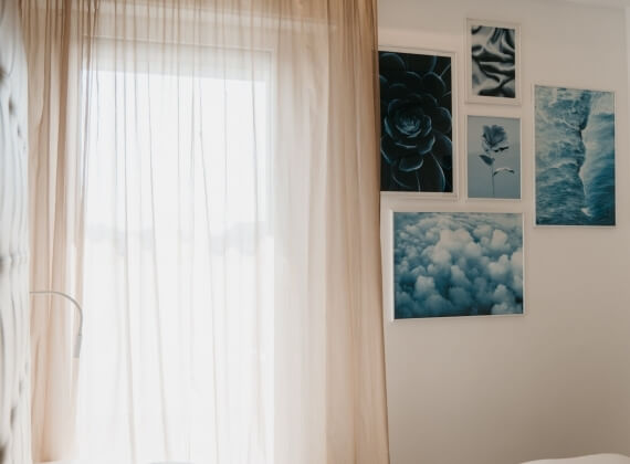 Una stanza con una finestra coperta da una tenda bianca e cinque fotografie in bianco e nero appese al muro.