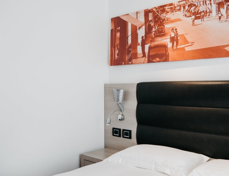 Camera d'albergo moderna con letto, comodino, lampada a muro e fotografia in seppia sopra il letto. Atmosfera pulita.