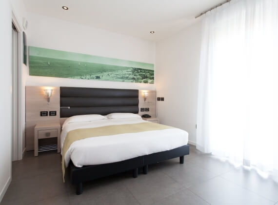 Camera d'albergo minimalista e serena, con letto matrimoniale, decorazioni bianche e accenti verdi, luce soffusa.