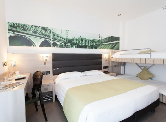 Hotelzimmer mit Wandgemälde der Triple Bridge, Doppelbett, Schreibtisch, Etagenbett und moderne Beleuchtung.