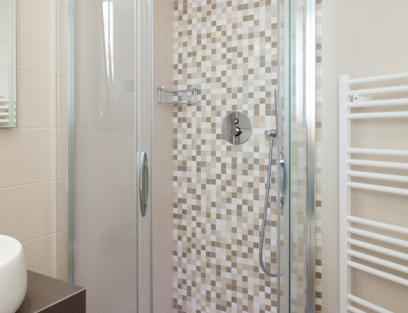 Modernes Badezimmer mit Dusche, Waschbecken und Handtuchhalter, gefliest in Brauntönen und Beige.