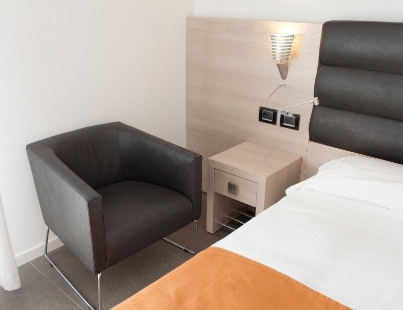 Ein modernes Hotelzimmer mit einem Bett, Nachttisch, Stuhl und einer minimalistischen Einrichtung in neutralen Farben.