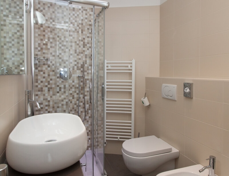 Ein sauberes Badezimmer mit Dusche, Toilette und Waschbecken, beige Fliesenwände und dunkle Fliesenböden.