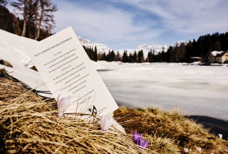 Una scena invernale serena con un foglio bianco parzialmente sepolto nell'erba secca e un lago ghiacciato sullo sfondo.