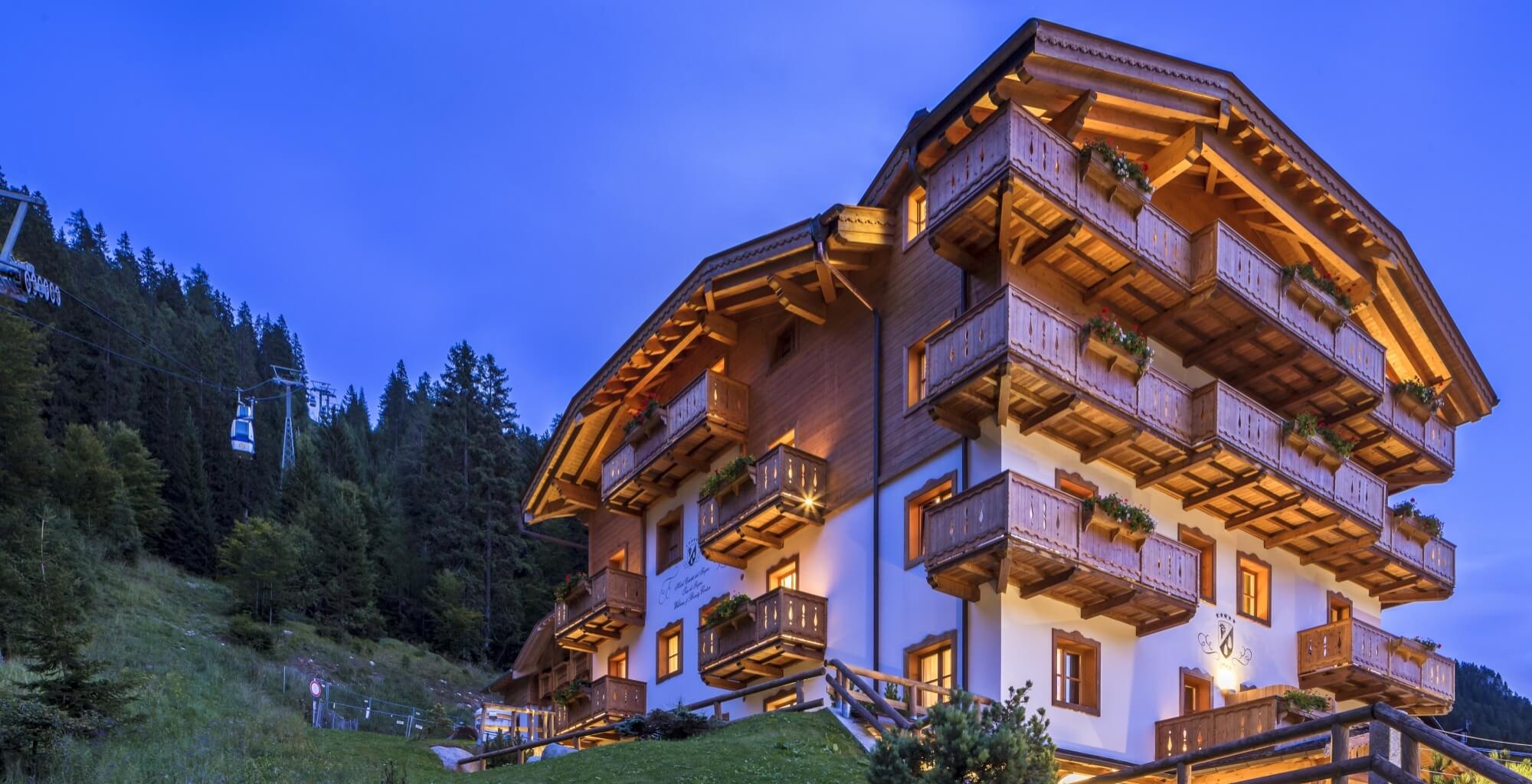 Ein mehrstöckiges Holzgebäude in den Bergen mit weißen und braunen Akzenten, umgeben von Bäumen und einem Skilift.