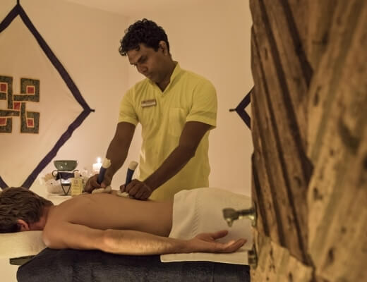 Mężczyzna otrzymuje masaż od terapeuty w spokojnym pomieszczeniu z białymi ścianami i świecą na stole.