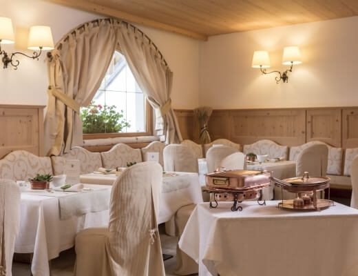 Interior of an elegant restaurant with cream walls, wooden accents, white tables, and copper serving dishes on a central table.