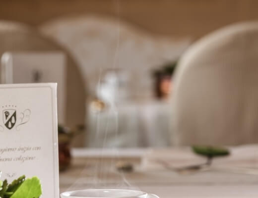 Partially obscured restaurant table with a menu card, green leaves, glass of water, and chairs in a bright setting.