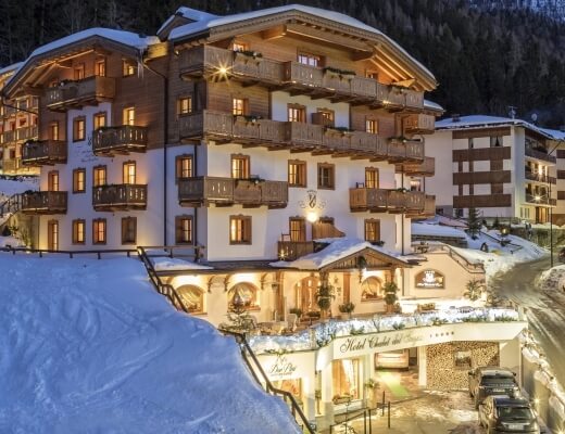 Scena invernale serena con un grande edificio bianco illuminato da luci calde, circondato da alberi coperti di neve.