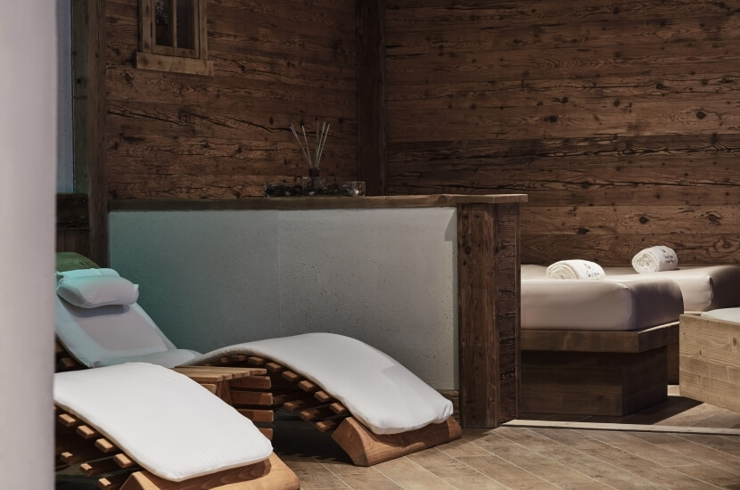 Ein ruhiger Raum mit zwei verstellbaren Liegen, einem Bett und einer Holzwand, die eine entspannende Atmosphäre schafft.