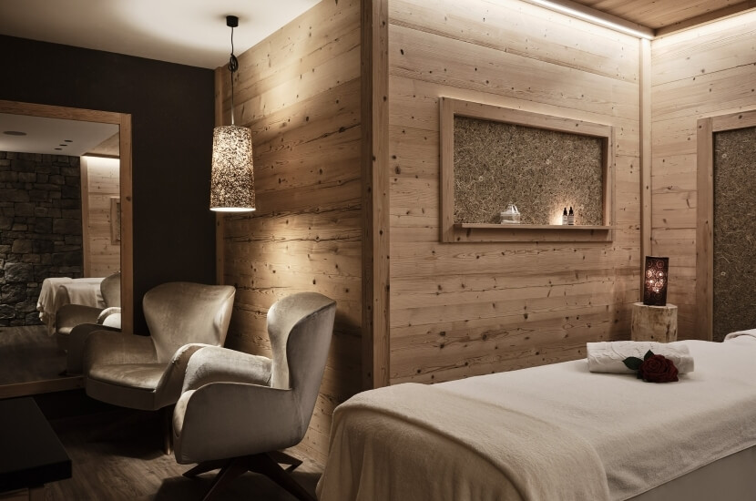 Ein ruhiger Spa-Raum mit warmem Licht, weißen Ledersesseln, einem Tisch mit einer Rose und Holz- sowie Steinelementen.