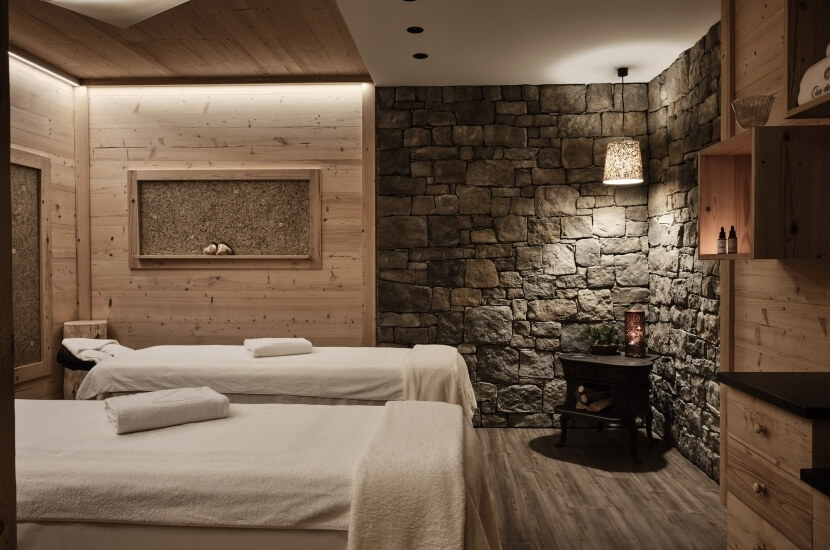 Ein ruhiger Spa-Raum mit zwei Massagetischen, einer Steinwand und sanfter Beleuchtung, die Entspannung ausstrahlt.