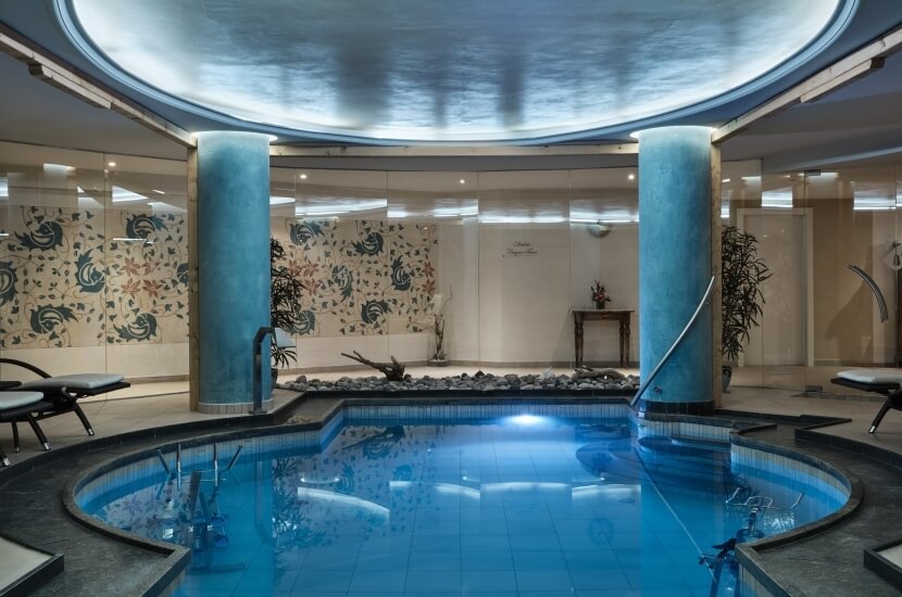 Ein ruhiger Innenpool mit kreisförmigem Design, Wasserfall, Liegen, Pflanzen und einer dekorativen Felswand.