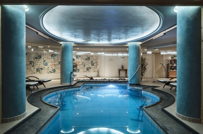 Luxuriöser Innenpoolbereich mit runder blauer Pool, Lounge-Stühlen und dekorativen Fliesen, umgeben von eleganten Säulen.