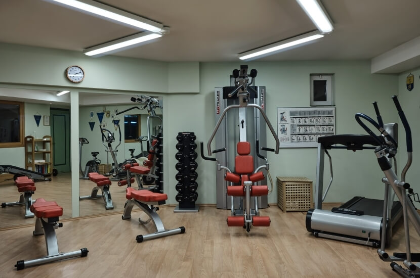 Interior of a home gym with an elliptical, weight bench, dumbbell rack, and a large weight-lifting machine against mint green walls.