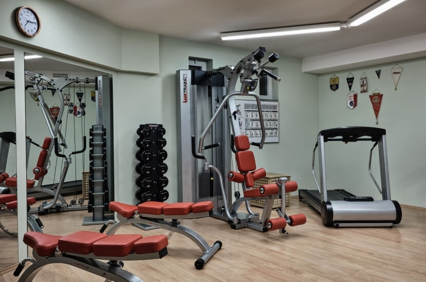 Home gym with weight machines, treadmill, wall clock, and sports equipment, featuring light green walls and wooden floor.