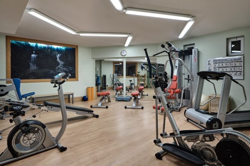 A spacious gym with exercise machines, free weights, a serene waterfall poster, seating area, and a clock on the wall.