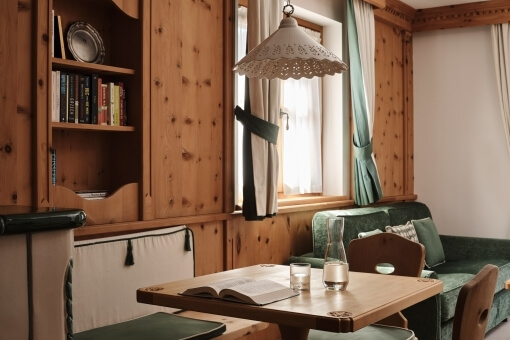 Cozy dining area with wooden table, green couch, and window, featuring candles, a vase, and wooden paneling.
