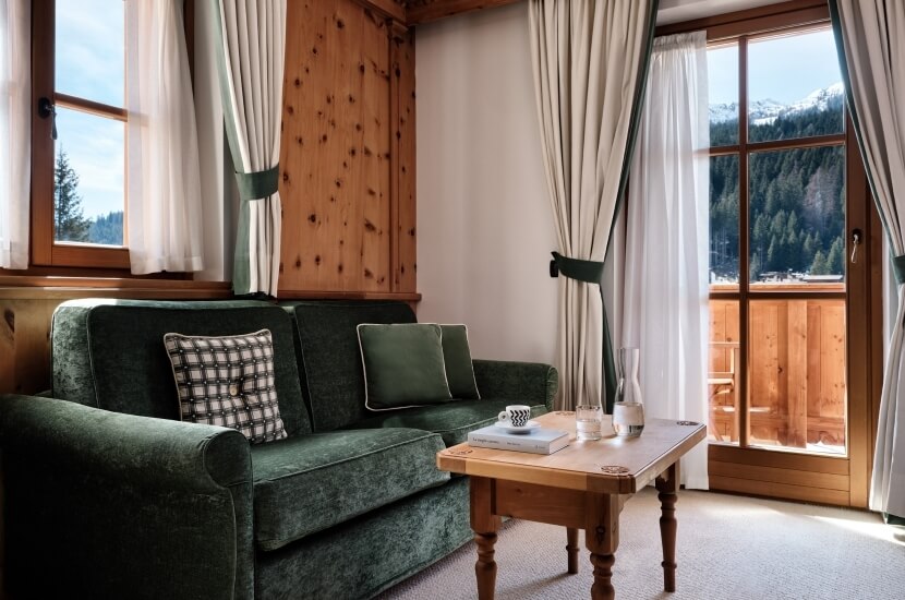 Soggiorno accogliente con divano verde, tavolino in legno e finestre che offrono vista sulle montagne.