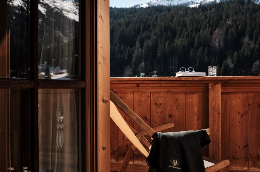 Una sedia e un tavolo di legno all'aperto, con un paesaggio di alberi e montagne sullo sfondo, trasmettono serenità.