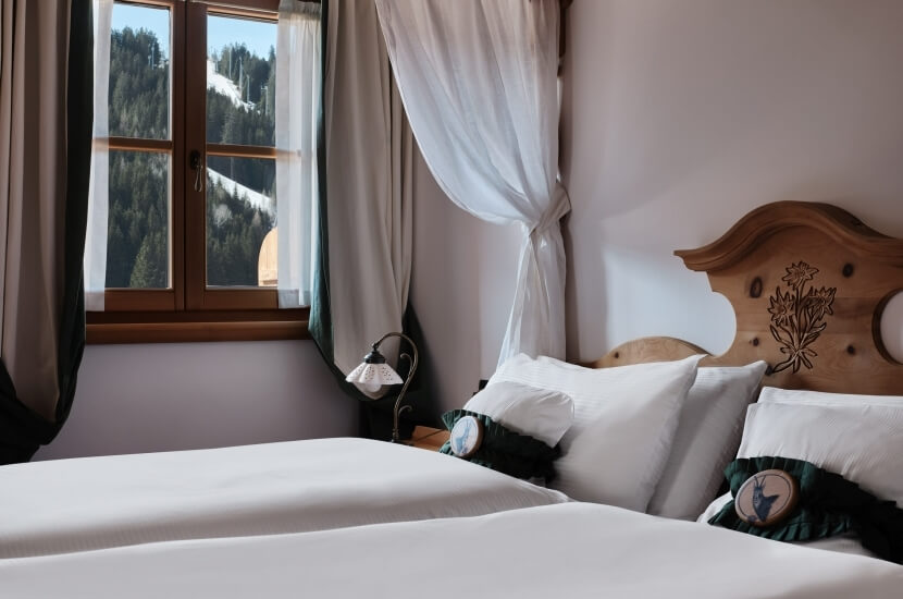 Camera serena con letto centrale, testata in legno chiaro, lenzuola bianche, cuscini verdi e vista su alberi e cielo blu.