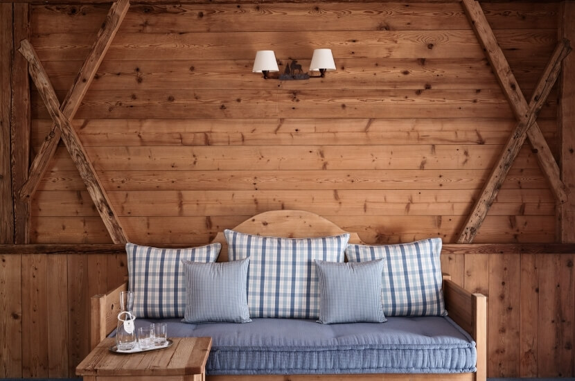 Wooden accent wall with hexagonal beams, a daybed with grey bedspread and patterned pillows, and a decorative table in a cozy cabin.