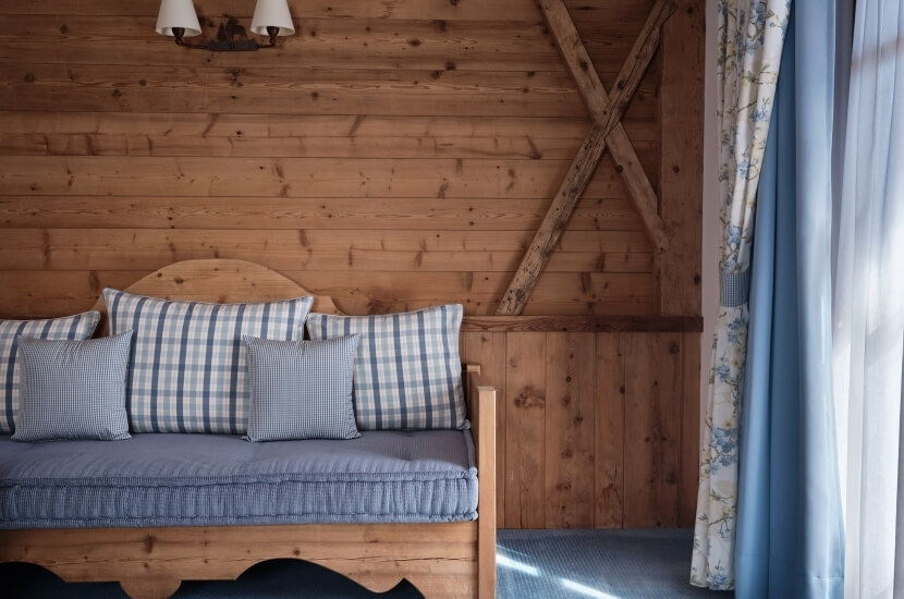 Cozy room with a daybed, blue cushions, floral curtains, and light wood walls, creating a serene atmosphere.