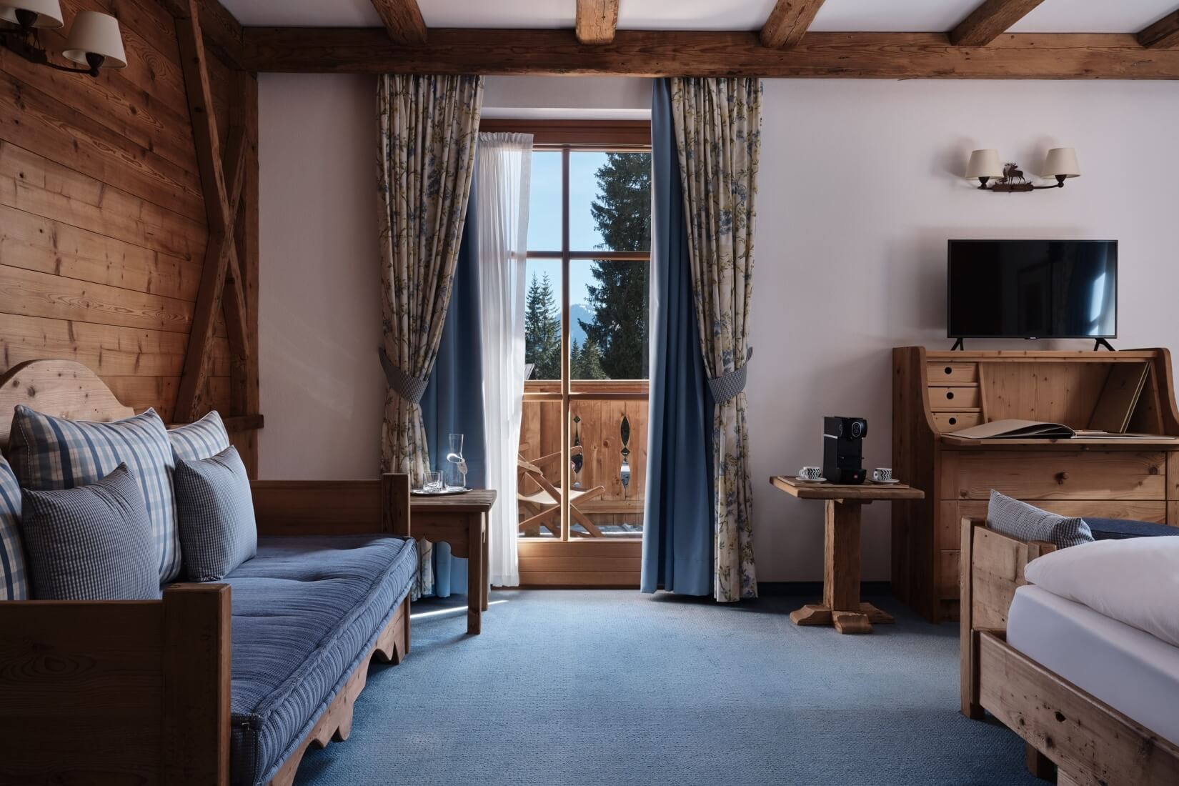 Przytulny pokój hotelowy z drewnianymi akcentami, dużym oknem i wygodną kanapą, stwarzający ciepłą atmosferę.