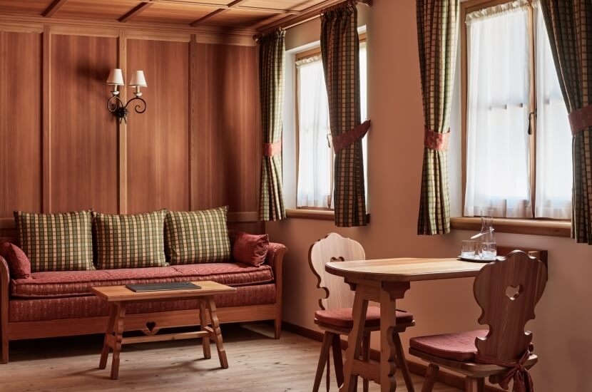 Gemütliches Wohnzimmer mit Essbereich, Holzverkleidung, rotem Sofa, runder Tisch und traditionellen Möbeln in warmen Farbtönen.