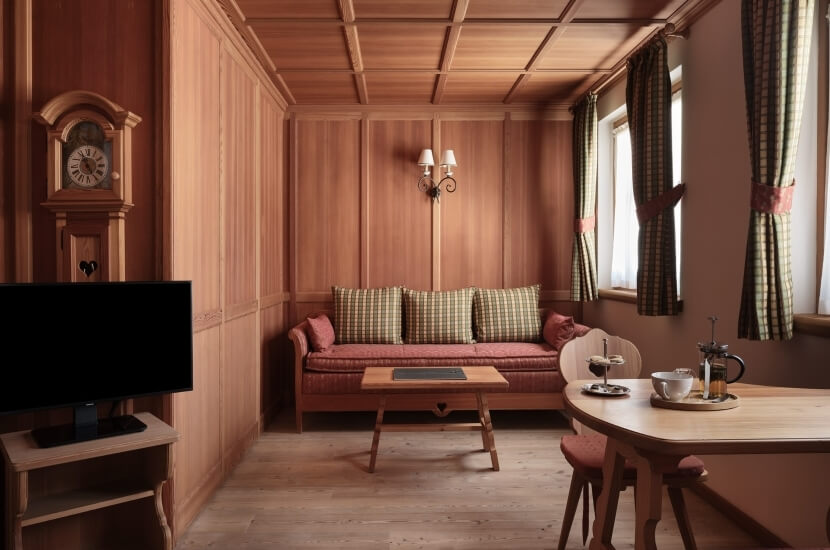 Gemütliches Wohnzimmer mit Essbereich, Holzsofa, Kaffeetisch, Großvateruhr und runder Esstisch, warmes Farbschema.