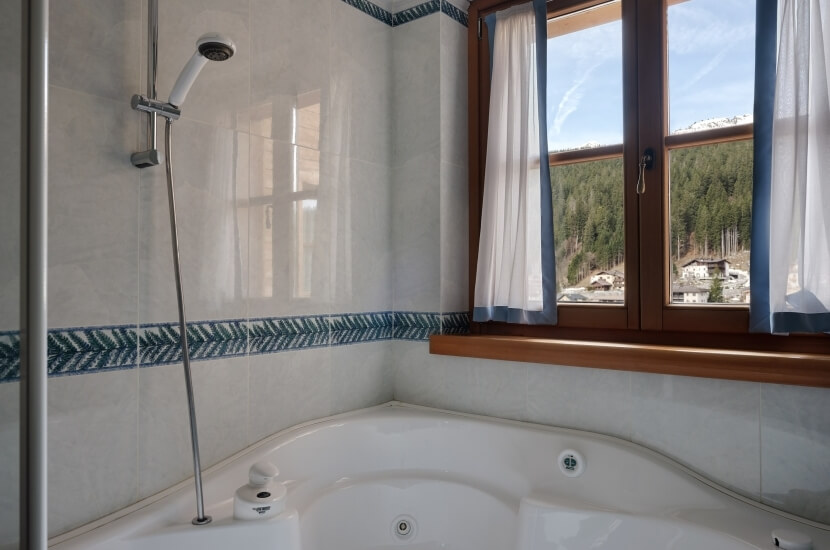 Serene bathroom with a sleek white bathtub, decorative tile border, and a view of a forest and snow-capped mountains.