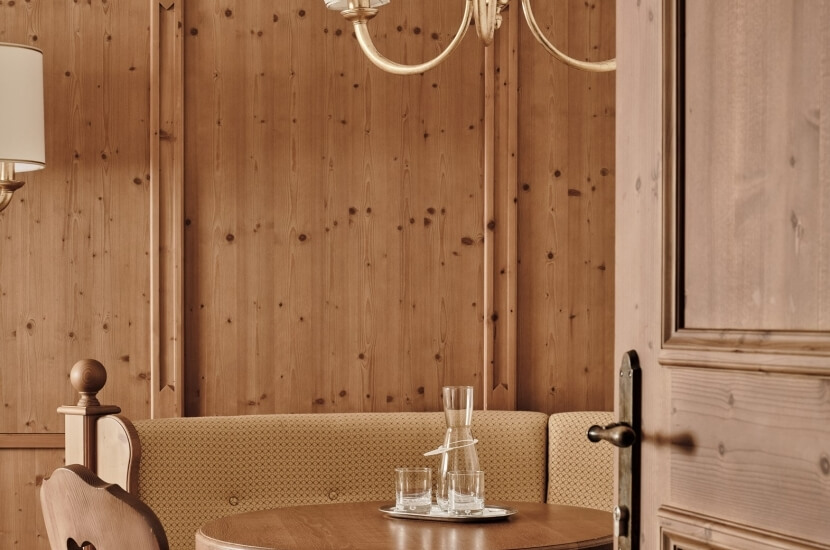 Cozy dining area with a wooden table, booth seating, lamp, and decanter with glasses against a light wood panel wall.