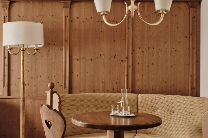 Cozy dining area with a round wooden table, upholstered bench, chandelier, and warm wood paneling, creating a relaxed atmosphere.