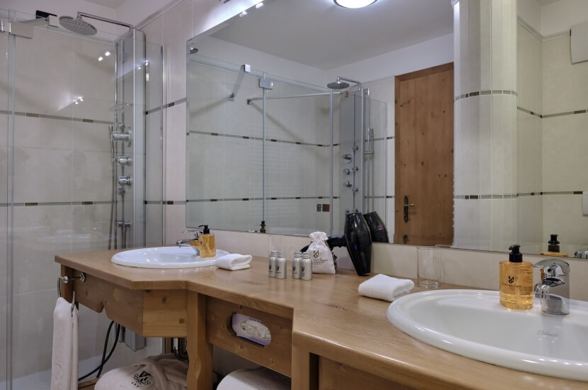 Modern bathroom with large mirror, two sinks, shower, and light wood accents, creating a bright and airy atmosphere.