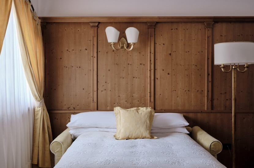 Serene bedroom with wood-paneled walls, a white comforter bed, elegant gold cushion, and warm lighting for a cozy atmosphere.